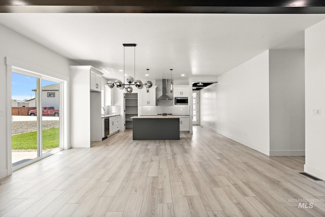 kitchen featuring wall chimney range hood, hanging light fixtures, a kitchen island, appliances with stainless steel finishes, and light hardwood / wood-style floors