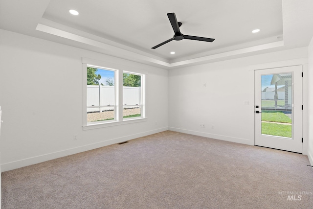 unfurnished room featuring a tray ceiling, ceiling fan, and light carpet