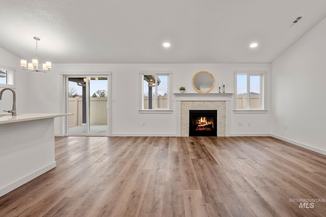 unfurnished living room with light wood-type flooring, a fireplace, a wealth of natural light, and an inviting chandelier