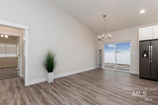 unfurnished dining area featuring a notable chandelier, lofted ceiling, and light wood-type flooring