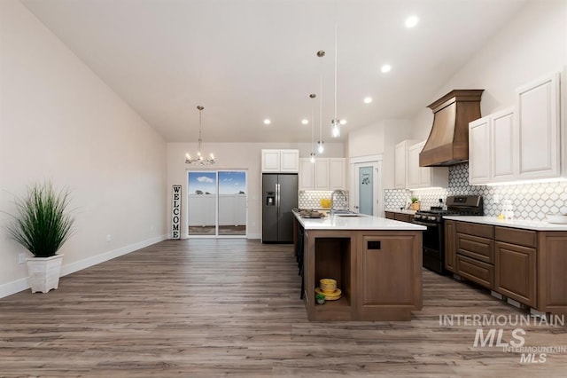 kitchen featuring pendant lighting, an island with sink, dark brown cabinetry, stainless steel appliances, and custom range hood