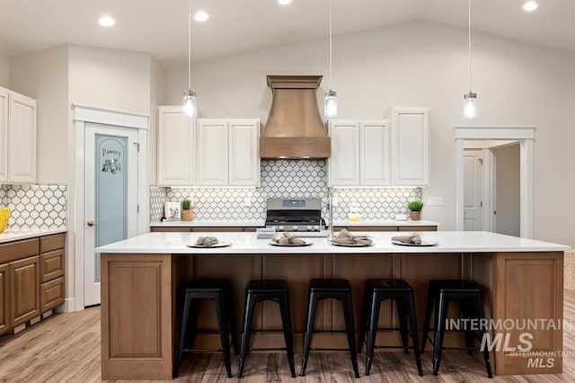 kitchen featuring a large island with sink, premium range hood, white cabinets, and stainless steel range