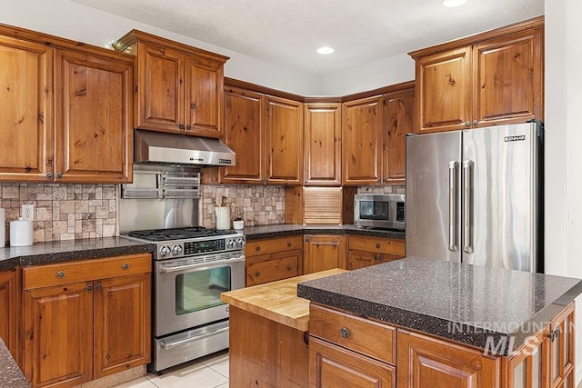 kitchen with stainless steel appliances, brown cabinets, under cabinet range hood, and tasteful backsplash