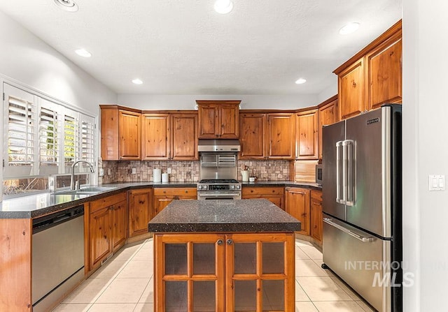 kitchen featuring light tile patterned floors, under cabinet range hood, a sink, appliances with stainless steel finishes, and brown cabinetry