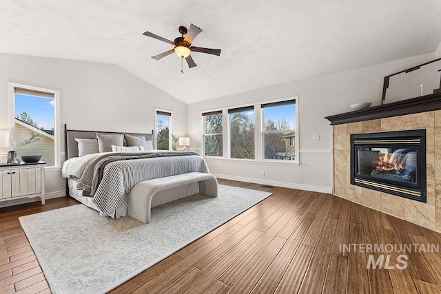 unfurnished bedroom with lofted ceiling, a textured ceiling, a tile fireplace, wood finished floors, and baseboards