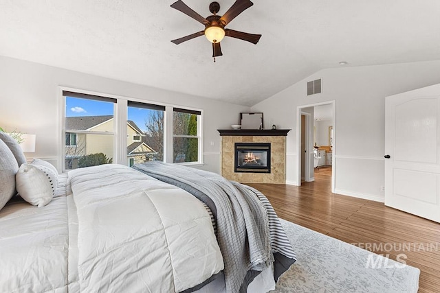 bedroom with baseboards, visible vents, a tiled fireplace, wood finished floors, and vaulted ceiling