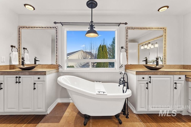 full bath featuring a soaking tub, two vanities, and a sink