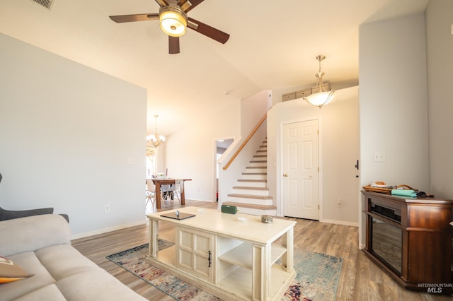 living room with ceiling fan with notable chandelier, lofted ceiling, stairway, and wood finished floors