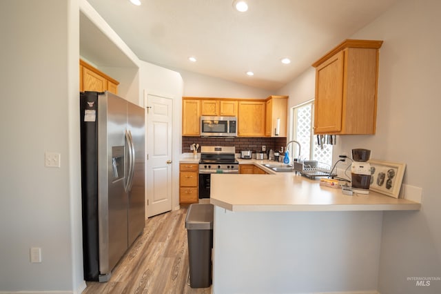 kitchen featuring a peninsula, a sink, light countertops, vaulted ceiling, and appliances with stainless steel finishes