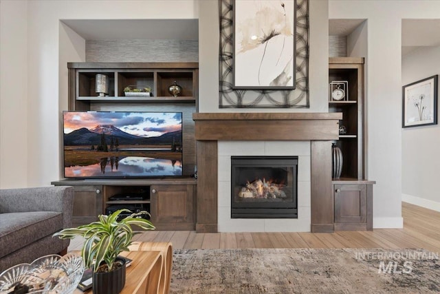 living room with wood-type flooring, a fireplace, and built in features