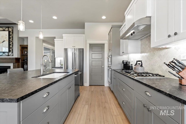 kitchen featuring wall chimney range hood, sink, hanging light fixtures, stainless steel appliances, and white cabinets