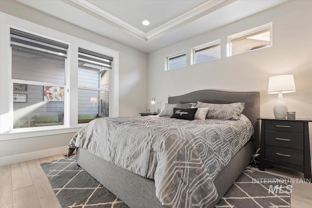 bedroom with hardwood / wood-style floors, ornamental molding, and a raised ceiling