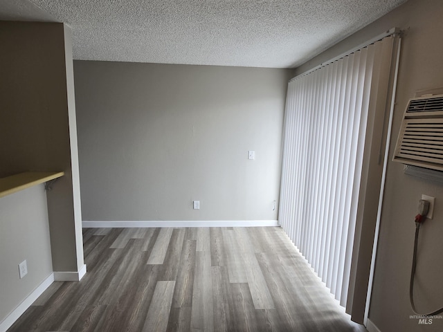 interior space with a textured ceiling, dark wood-type flooring, and an AC wall unit