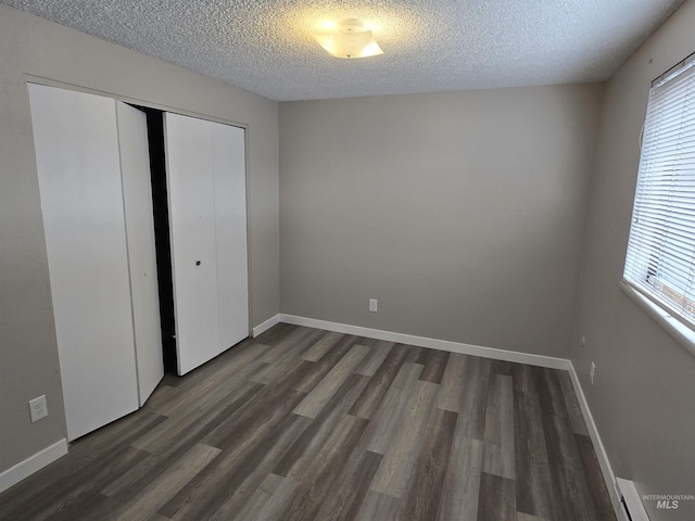 unfurnished bedroom featuring dark hardwood / wood-style flooring, a baseboard heating unit, a textured ceiling, and a closet