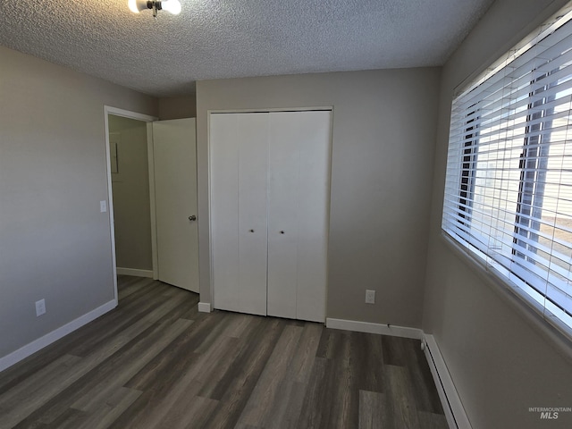 unfurnished bedroom featuring baseboard heating, dark wood-type flooring, a textured ceiling, and a closet