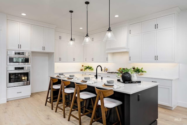 kitchen featuring double oven, white cabinets, light countertops, and a center island with sink