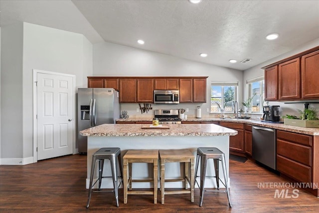 kitchen with stainless steel appliances, lofted ceiling, a kitchen breakfast bar, a sink, and a center island