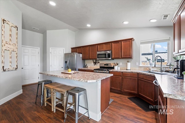 kitchen featuring appliances with stainless steel finishes, a center island, lofted ceiling, a breakfast bar, and dark wood-style floors