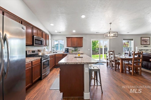 kitchen featuring appliances with stainless steel finishes, a textured ceiling, a kitchen breakfast bar, dark wood-style floors, and a kitchen island
