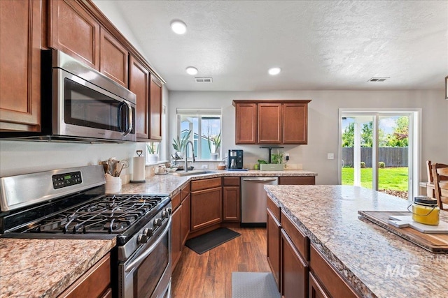 kitchen featuring stainless steel appliances, a sink, dark wood finished floors, brown cabinetry, and a textured ceiling