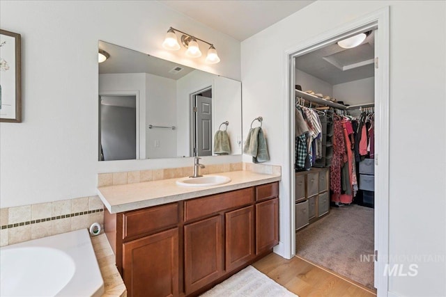 full bathroom featuring a walk in closet, vanity, a garden tub, and wood finished floors