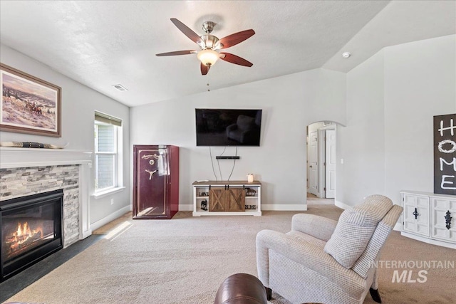 carpeted living area featuring lofted ceiling, a ceiling fan, baseboards, and a stone fireplace