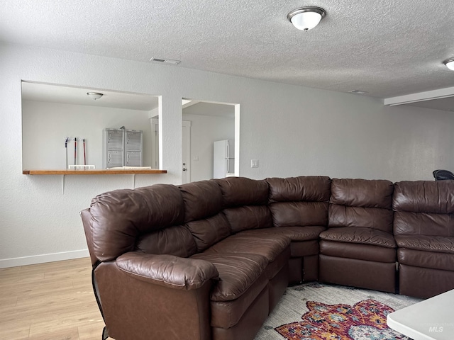 living area featuring visible vents, baseboards, a textured ceiling, and wood finished floors