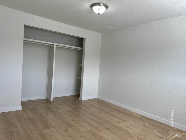 unfurnished bedroom featuring a closet, baseboards, light wood-style floors, and a textured ceiling