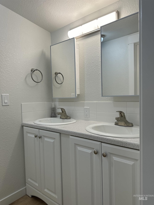 bathroom with a textured ceiling, double vanity, decorative backsplash, and a sink