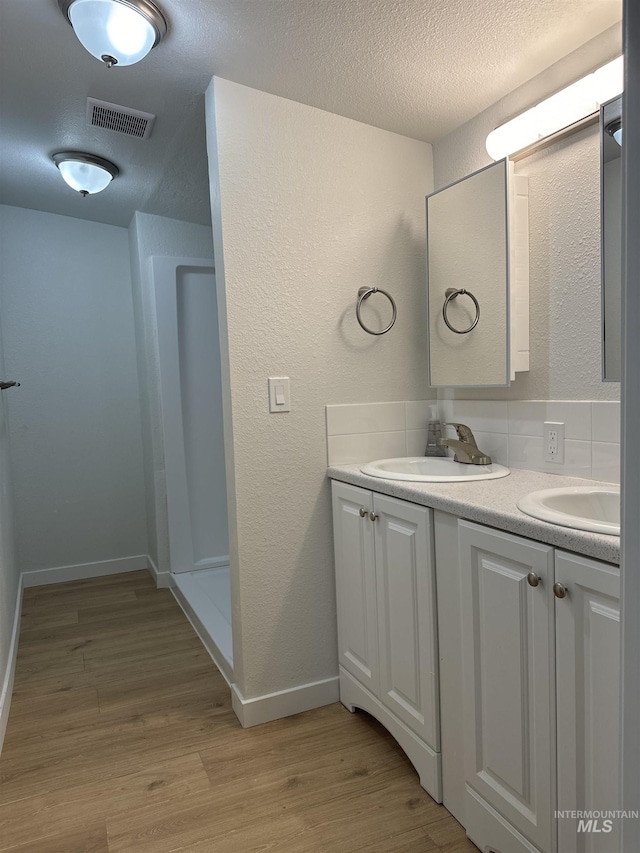 full bathroom with visible vents, a sink, a textured ceiling, and wood finished floors