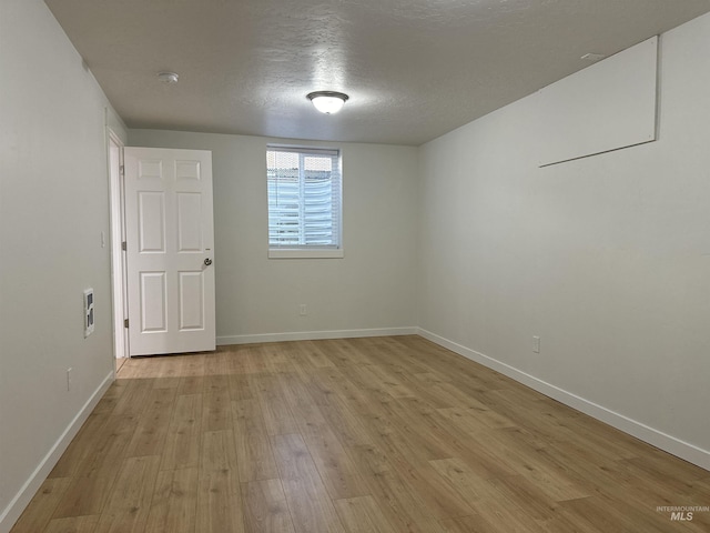 unfurnished room with a textured ceiling, light wood-type flooring, and baseboards