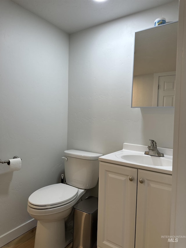 bathroom featuring baseboards, toilet, wood finished floors, and vanity