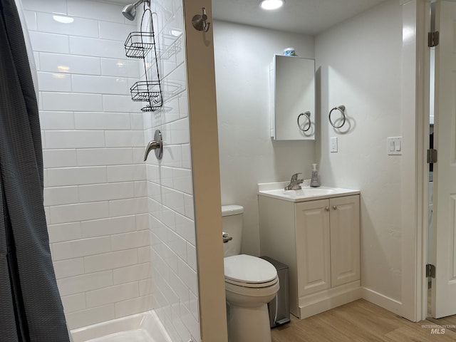 bathroom featuring toilet, tiled shower, vanity, and wood finished floors