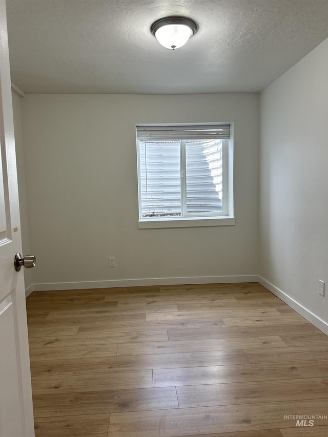 unfurnished room with light wood finished floors, a textured ceiling, and baseboards