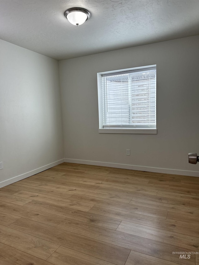 empty room featuring light wood-type flooring, baseboards, and a textured ceiling