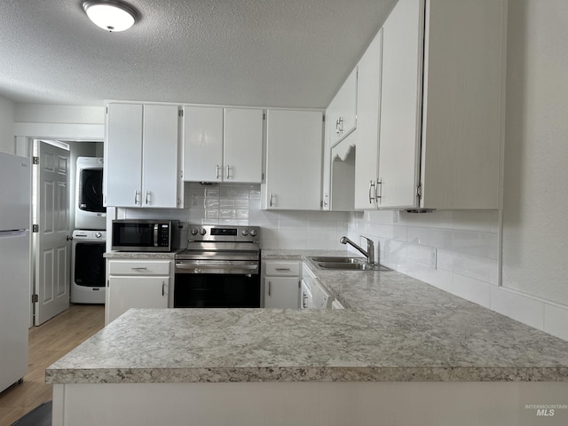 kitchen with light countertops, stacked washer and dryer, light wood-style floors, stainless steel appliances, and a sink