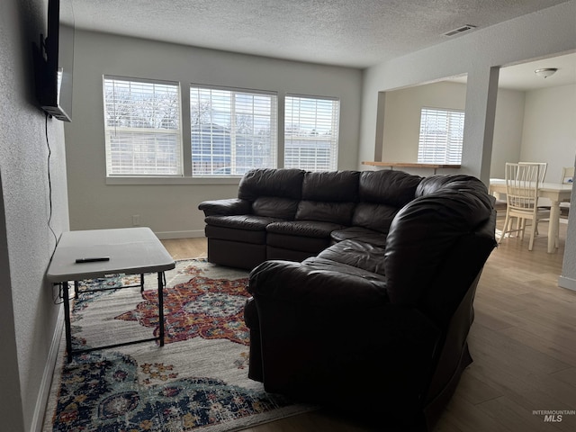 living room with wood finished floors, baseboards, visible vents, a textured ceiling, and a textured wall