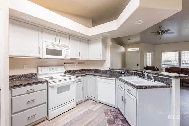 kitchen with a peninsula, white appliances, a sink, and dark countertops