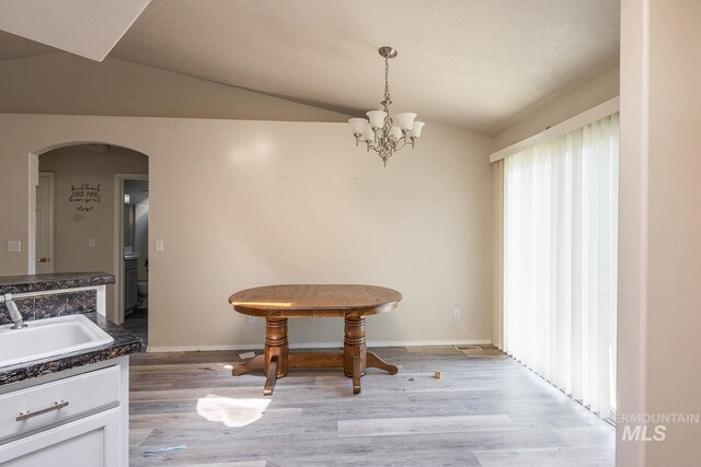 dining space featuring arched walkways, lofted ceiling, a notable chandelier, and light wood-style flooring