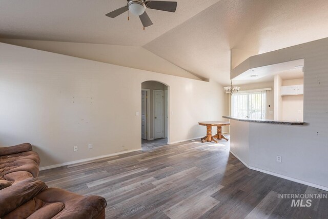 living room featuring vaulted ceiling, wood finished floors, ceiling fan with notable chandelier, arched walkways, and baseboards
