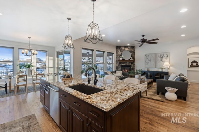 kitchen featuring sink, a stone fireplace, a kitchen island with sink, light hardwood / wood-style floors, and decorative light fixtures