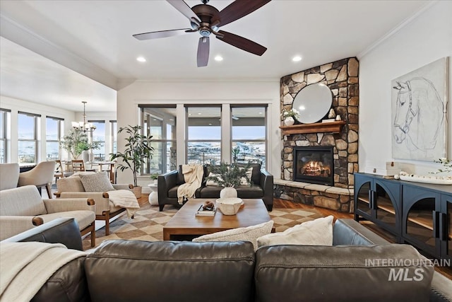 living room with crown molding, a stone fireplace, and ceiling fan with notable chandelier