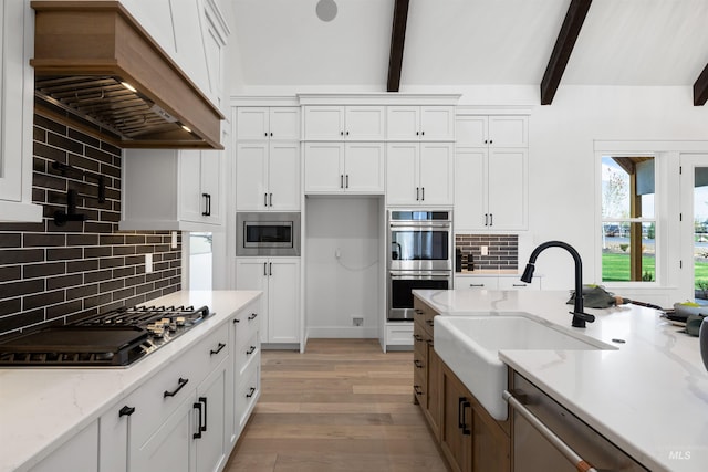 kitchen with tasteful backsplash, a sink, light wood finished floors, custom range hood, and appliances with stainless steel finishes