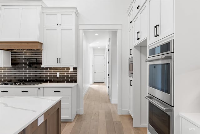 kitchen with stainless steel appliances, light wood-type flooring, baseboards, white cabinetry, and decorative backsplash