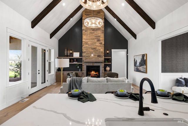 living area with a stone fireplace, beamed ceiling, a chandelier, light wood-style flooring, and high vaulted ceiling