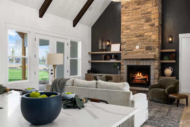living area with wood finished floors, a stone fireplace, beam ceiling, and high vaulted ceiling