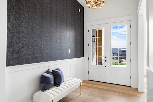 doorway to outside featuring french doors, an inviting chandelier, a wainscoted wall, and hardwood / wood-style flooring