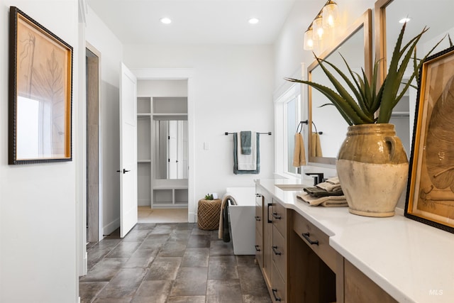 bathroom featuring a freestanding bath, vanity, stone finish flooring, baseboards, and recessed lighting