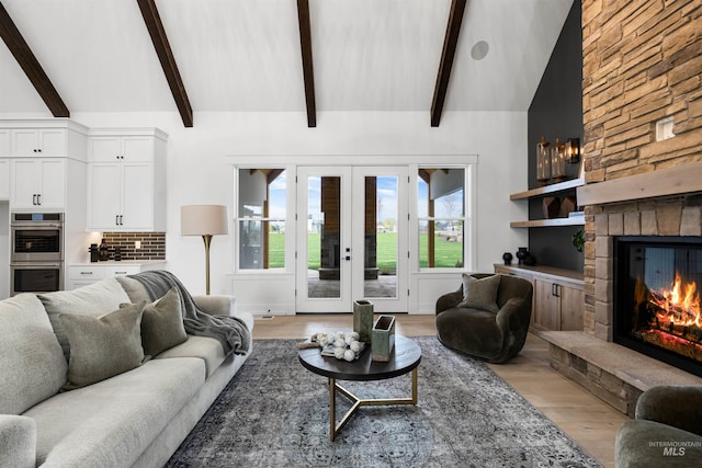living room with a stone fireplace, french doors, beamed ceiling, light wood-style flooring, and high vaulted ceiling