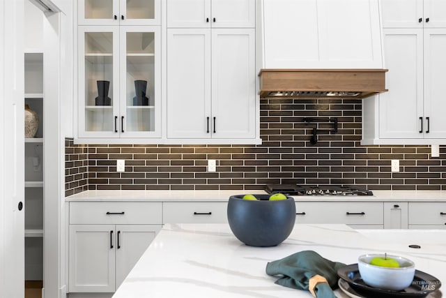 kitchen featuring light stone counters, glass insert cabinets, stainless steel gas cooktop, tasteful backsplash, and white cabinetry